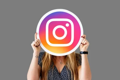 Asmuo laiko Instagram logotipą prieš veidą pilkame fone, simbolizuodamas socialinių tinklų identitetą.